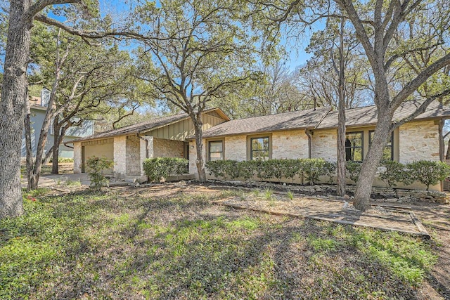 view of front of house featuring board and batten siding, an attached garage, stone siding, and driveway