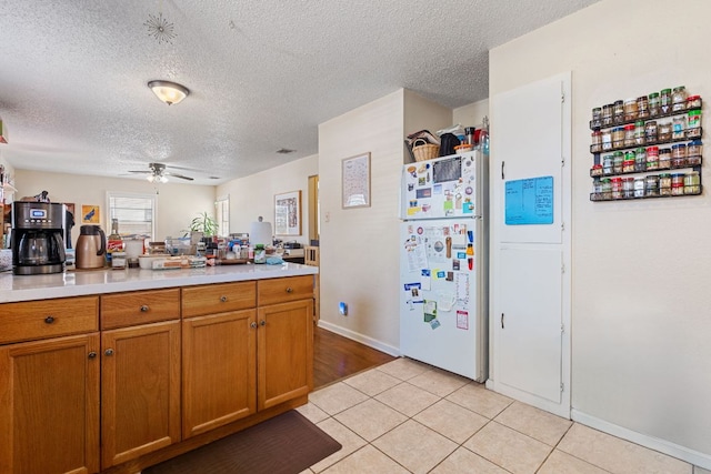 1513 Ruth Ave, Austin, TX 78757 - kitchen featuring a ceiling fan, freestanding refrigerator, light tile patterned flooring, brown cabinetry, and light countertops