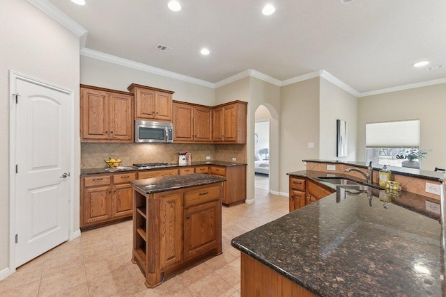 2812 Prosperity, Leander, TX 78641 - kitchen featuring stainless steel appliances, a center island with sink, a sink, arched walkways, and brown cabinetry