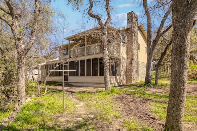 back of house with a balcony, a sunroom, and a chimney