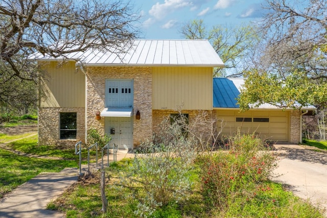 view of front of property featuring a standing seam roof, concrete driveway, a garage, stone siding, and metal roof