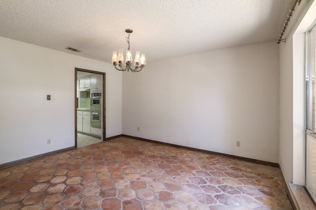 unfurnished room with a textured ceiling, baseboards, visible vents, and a chandelier