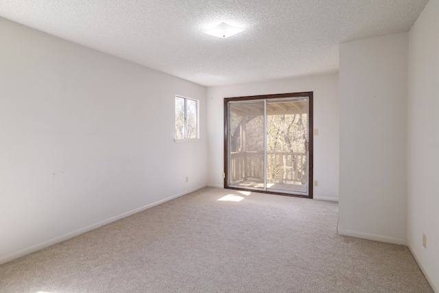 spare room with light colored carpet, baseboards, and a textured ceiling