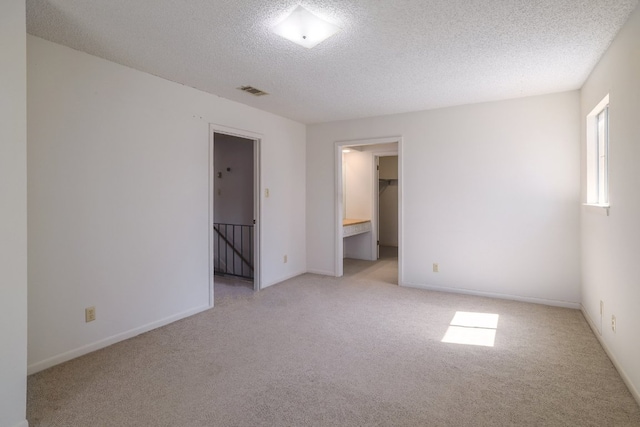 unfurnished bedroom featuring baseboards, a textured ceiling, a walk in closet, and carpet