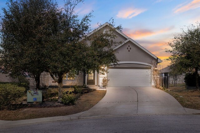 obstructed view of property with stucco siding, concrete driveway, an attached garage, and fence