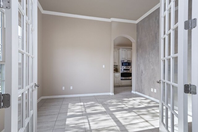 spare room featuring french doors, arched walkways, baseboards, and ornamental molding