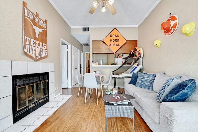 living room featuring visible vents, a tile fireplace, a ceiling fan, and crown molding