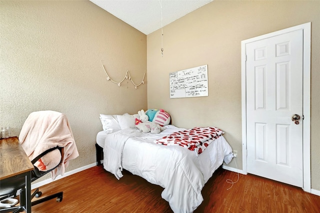 bedroom with vaulted ceiling, baseboards, and wood finished floors