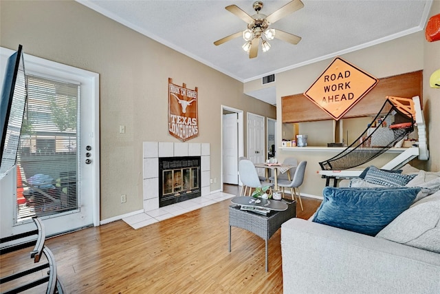 living area featuring visible vents, crown molding, a fireplace, wood finished floors, and a ceiling fan