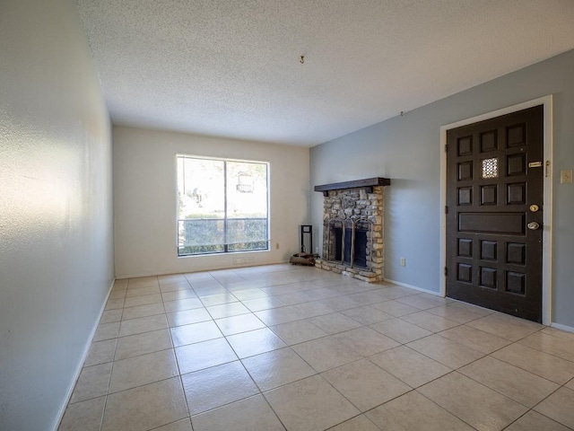 unfurnished living room with light tile patterned floors, a stone fireplace, a textured ceiling, and baseboards