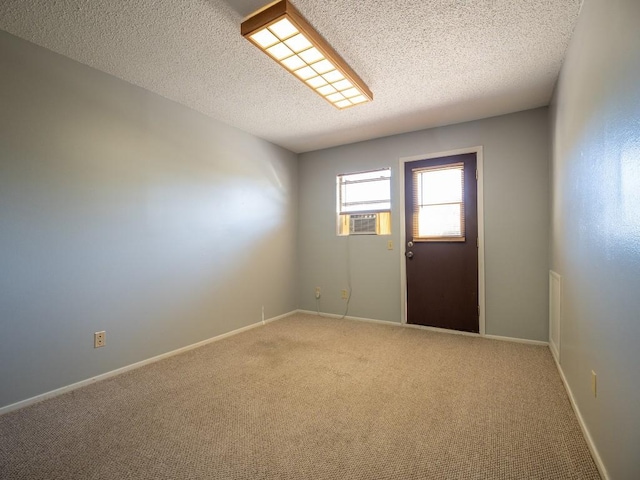 empty room featuring carpet flooring, cooling unit, baseboards, and a textured ceiling