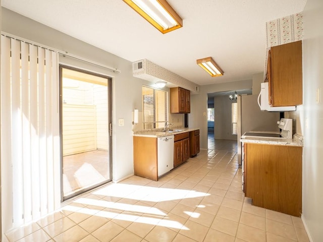 kitchen with dishwasher, light countertops, light tile patterned floors, and brown cabinetry