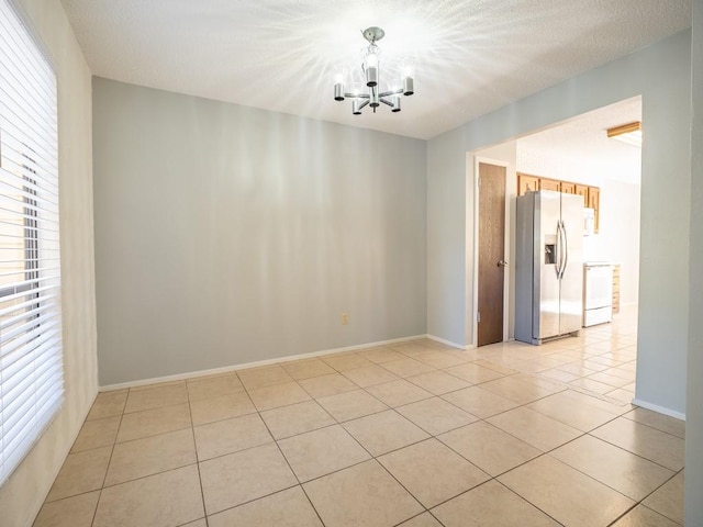 empty room with a textured ceiling, light tile patterned floors, baseboards, and a chandelier