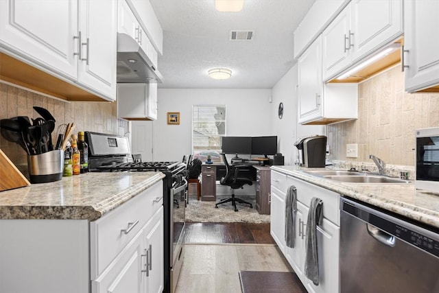 6705 Skynook Dr, Austin, TX 78745 - kitchen with appliances with stainless steel finishes, under cabinet range hood, wood finished floors, a desk, and decorative backsplash