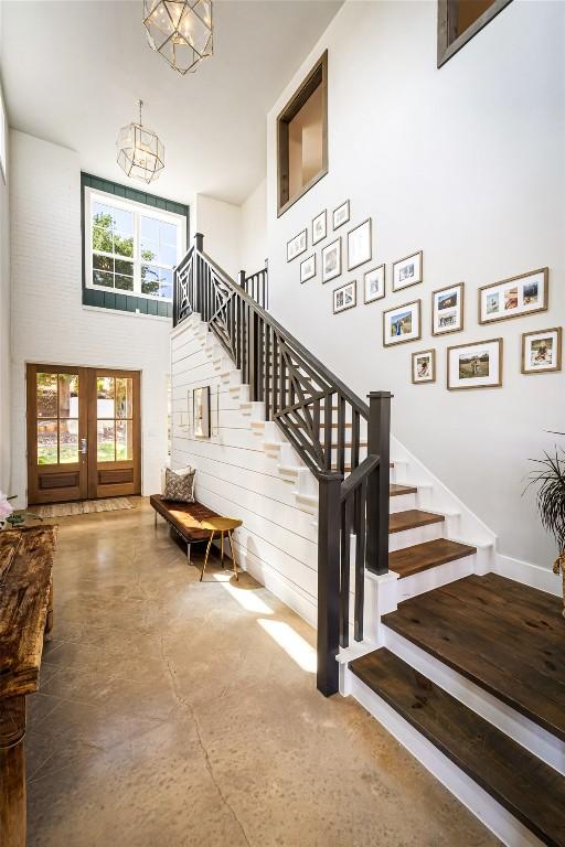 stairs featuring a chandelier, concrete flooring, a high ceiling, and french doors