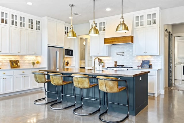 kitchen with washing machine and clothes dryer, visible vents, black microwave, an island with sink, and high quality fridge