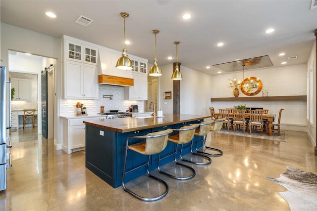 kitchen with premium range hood, visible vents, a sink, white cabinetry, and butcher block counters