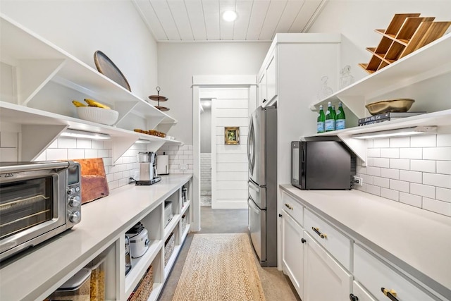 kitchen with white cabinetry, open shelves, backsplash, and freestanding refrigerator