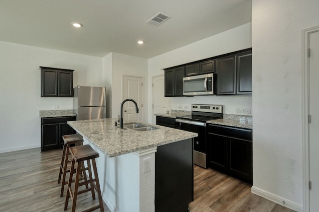 kitchen with visible vents, a center island with sink, a sink, wood finished floors, and appliances with stainless steel finishes