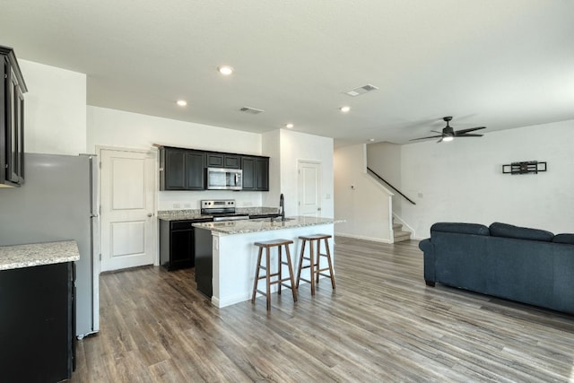 kitchen featuring open floor plan, an island with sink, dark wood-style floors, stainless steel appliances, and a sink