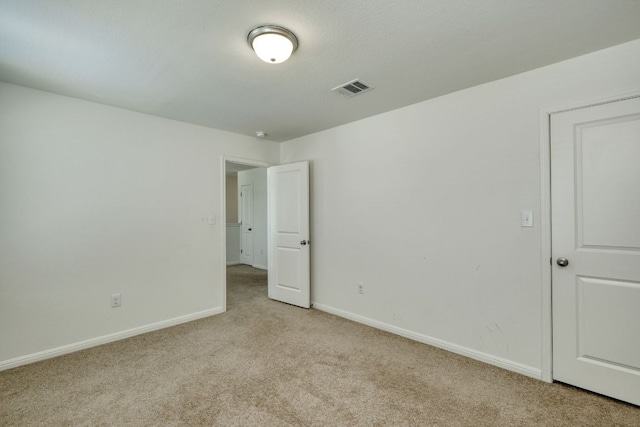 empty room featuring visible vents, light colored carpet, and baseboards