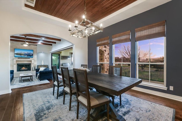 dining area with baseboards, wood ceiling, a warm lit fireplace, arched walkways, and wood-type flooring