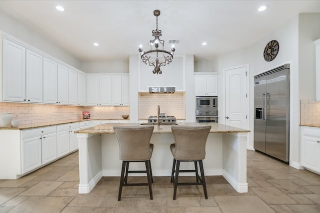 kitchen featuring stone tile floors, light stone countertops, visible vents, a center island with sink, and built in appliances