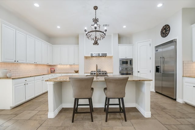211 Jack Nicklaus Dr, Austin, TX 78738 - kitchen featuring built in appliances, a center island with sink, decorative backsplash, light stone countertops, and a breakfast bar