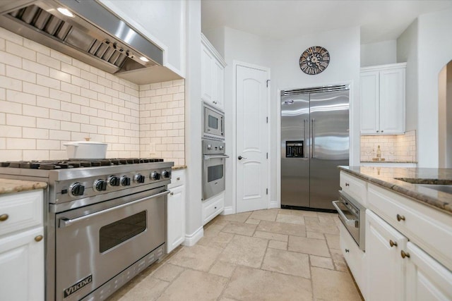 kitchen featuring built in appliances, custom exhaust hood, stone tile flooring, and white cabinets