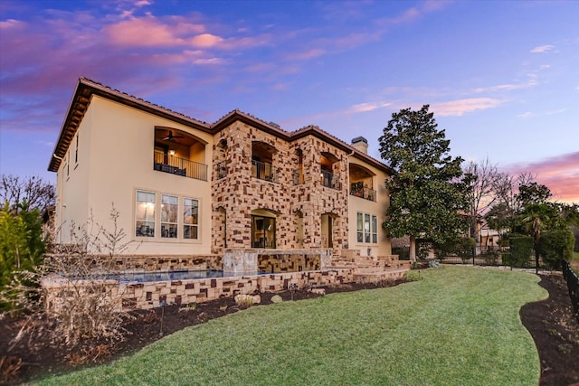 rear view of property featuring stucco siding, a chimney, a yard, a balcony, and stone siding