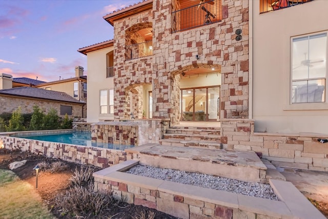 exterior space featuring a balcony, an outdoor pool, and stone siding