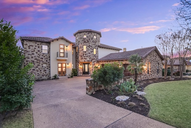 mediterranean / spanish home with stucco siding, driveway, stone siding, a yard, and a tiled roof