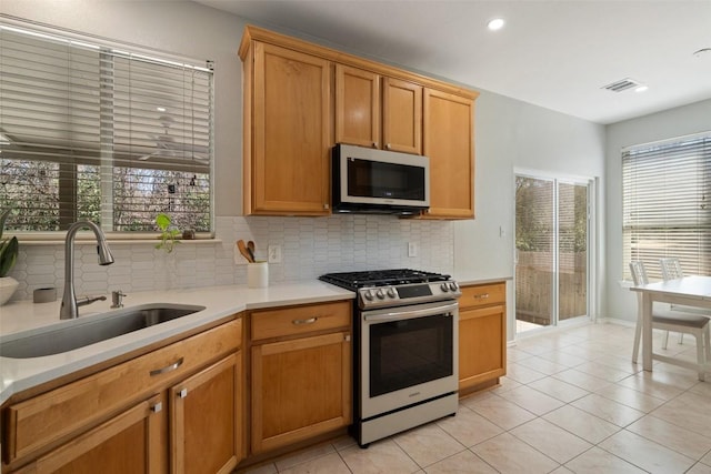 kitchen featuring stainless steel gas range oven, a sink, decorative backsplash, light countertops, and light tile patterned floors