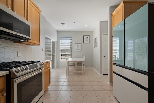 kitchen featuring light tile patterned floors, visible vents, stainless steel gas range, decorative backsplash, and light countertops