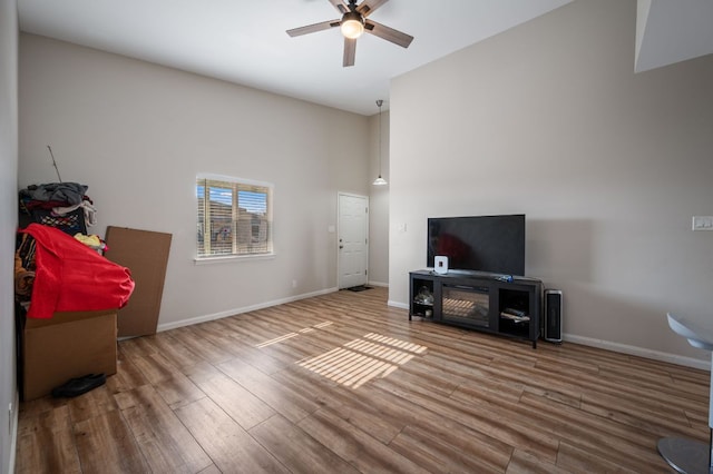 living area with wood finished floors, baseboards, a towering ceiling, and ceiling fan