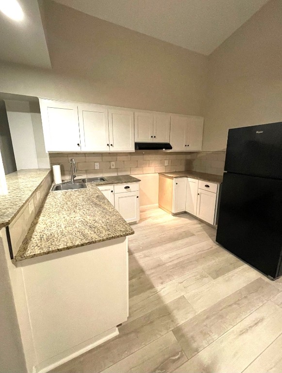 kitchen with light wood finished floors, decorative backsplash, freestanding refrigerator, white cabinets, and a sink