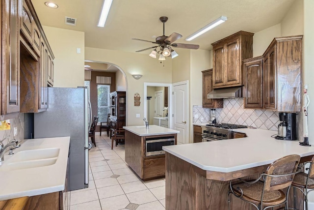 200 Hillside Dr, Dripping Springs, TX 78620 - kitchen with stainless steel appliances, exhaust hood, ceiling fan, tasteful backsplash, and an island with sink