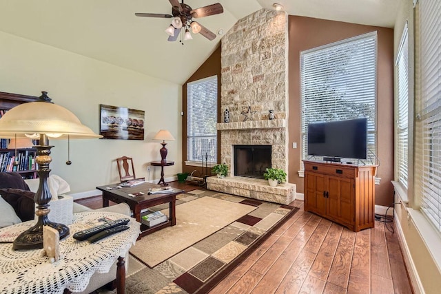 living room with baseboards, hardwood / wood-style flooring, a ceiling fan, and a stone fireplace