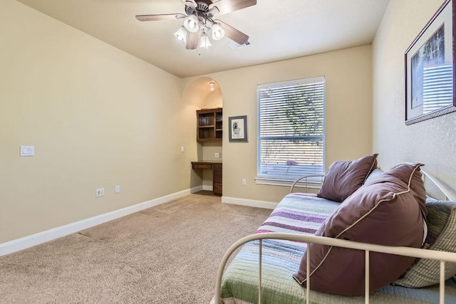 living area featuring baseboards, light carpet, a ceiling fan, and plenty of natural light
