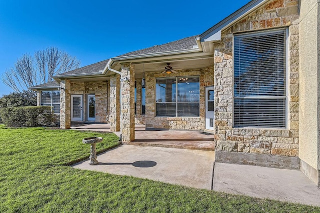 exterior space with ceiling fan, roof with shingles, a yard, and stone siding