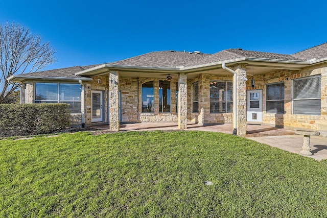 rear view of property featuring a yard, stone siding, a shingled roof, and a patio area