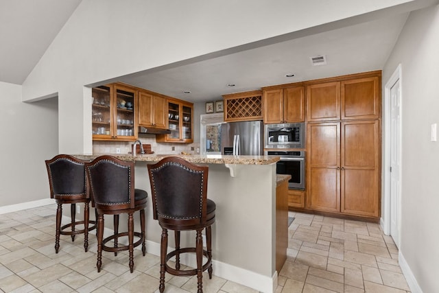6702 Elfland Dr, Austin, TX 78746 - kitchen featuring appliances with stainless steel finishes, brown cabinets, light stone counters, stone tile flooring, and recessed lighting
