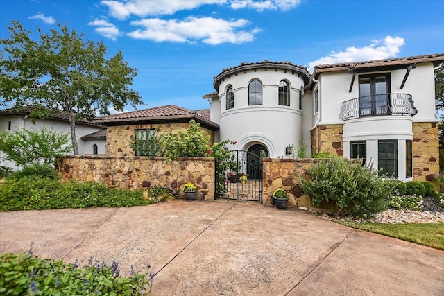 mediterranean / spanish home with a balcony, a gate, stucco siding, stone siding, and a tile roof
