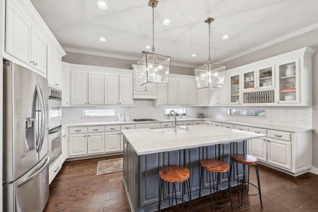 kitchen featuring an island with sink, a sink, dark wood finished floors, stainless steel appliances, and white cabinets