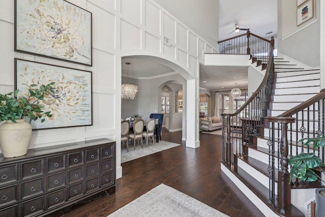 entryway with dark wood-style floors, stairway, arched walkways, a high ceiling, and a chandelier