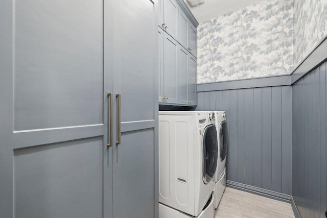 laundry area with washer and dryer, light wood-style flooring, cabinet space, and wainscoting