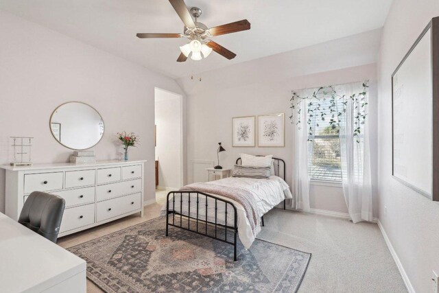 bedroom with ceiling fan, vaulted ceiling, baseboards, and light carpet