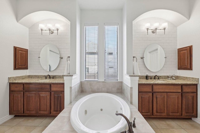 full bath featuring a notable chandelier, a tub with jets, a wealth of natural light, and a sink
