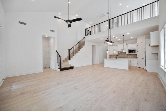 1601 Cardinal Ln, Round Rock, TX 78681 - unfurnished living room with a towering ceiling, light wood-style flooring, stairway, a ceiling fan, and baseboards