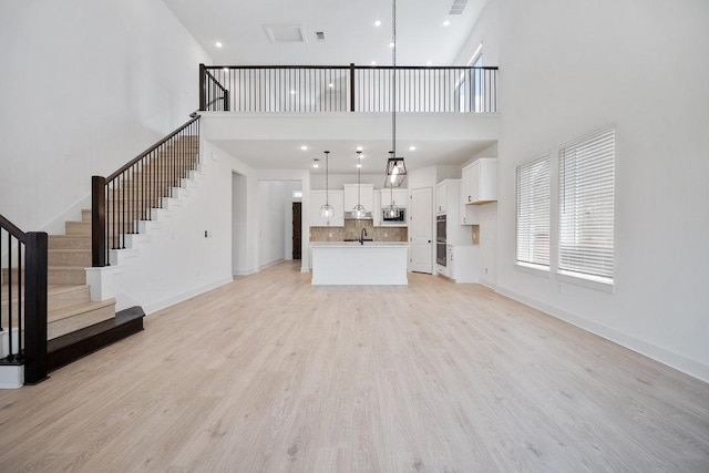 1601 Cardinal Ln, Round Rock, TX 78681 - unfurnished living room with a towering ceiling, stairs, light wood finished floors, a sink, and baseboards